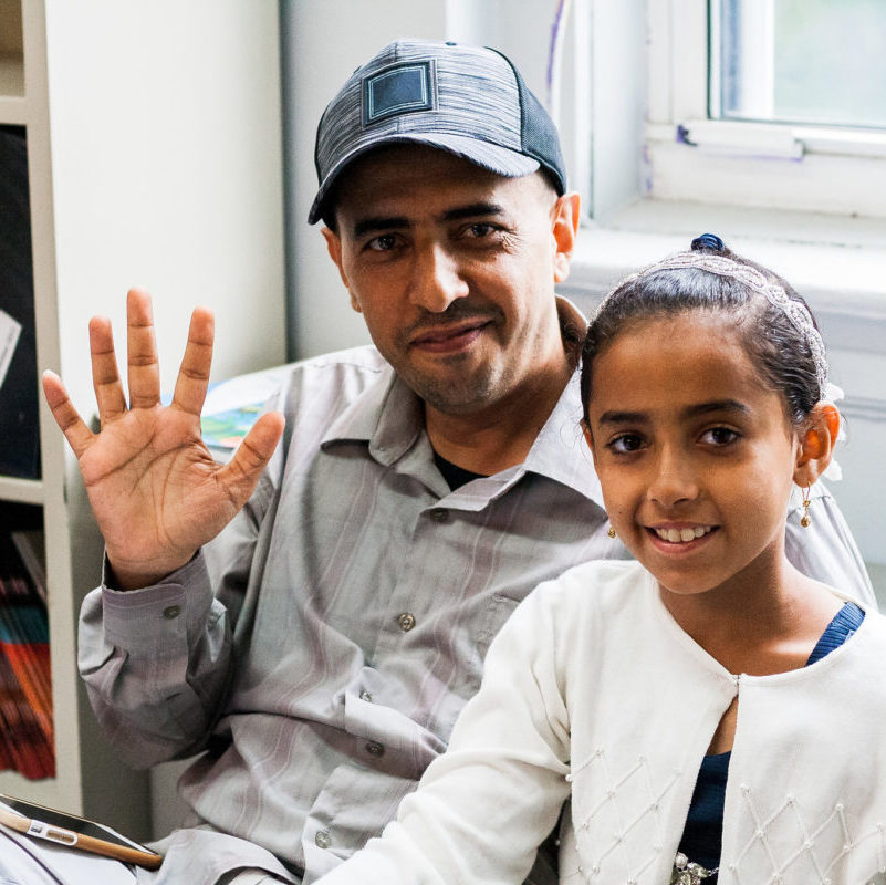 Smiling father holding out his hand in a wave, and his daughter is next to him.